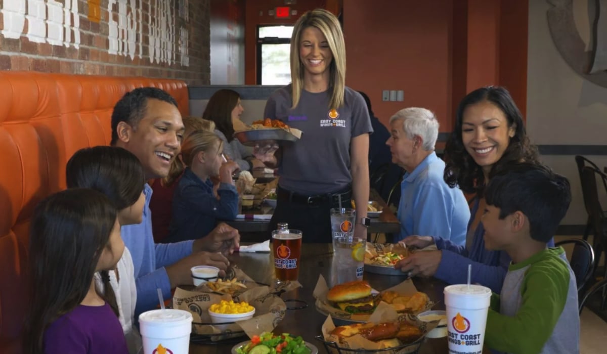 A Server Bringing Food To A Table Of Guests At East Coast Wings + Grill