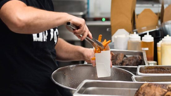 Fast-food worker putting fries in a basket.