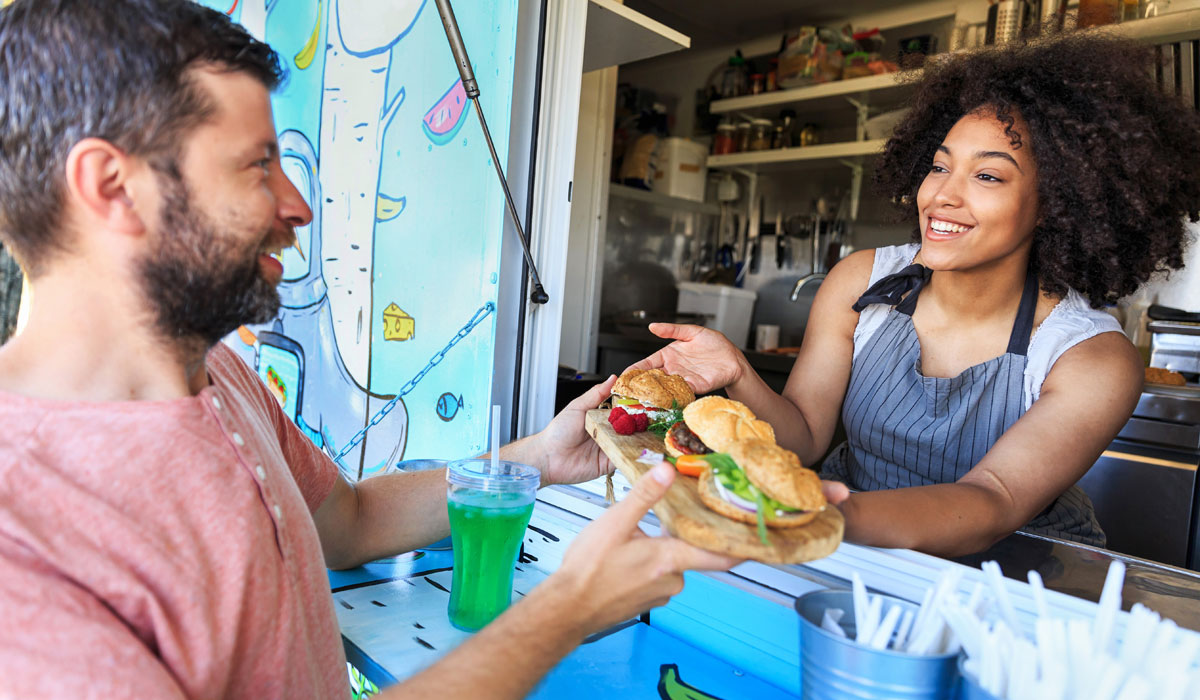 A Woman Hands A Customer Food Through The Window Of A Food Truck