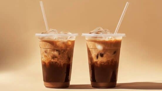 Two plastic cup mockup of cold coffee with ice cubes and straw on aesthetic beige background.