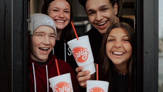 Swig employees smiling in the drive-thru window with drinks.